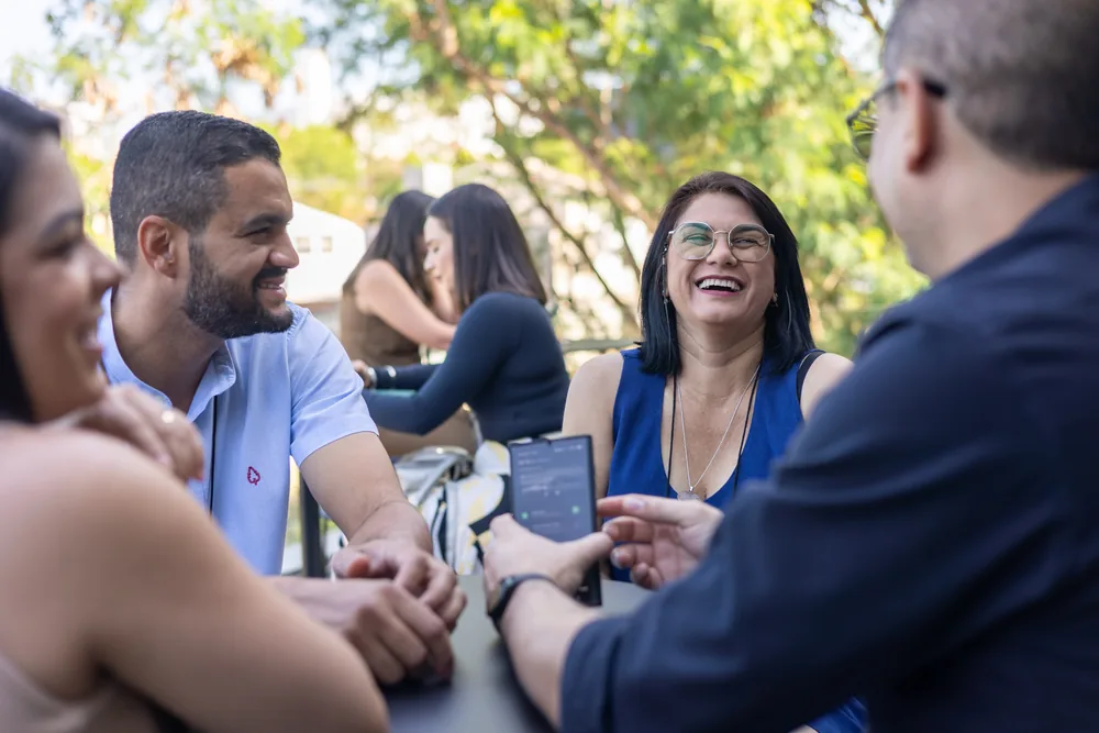 Participantes conversam e riem juntos em volta de uma mesa ao ar livre.